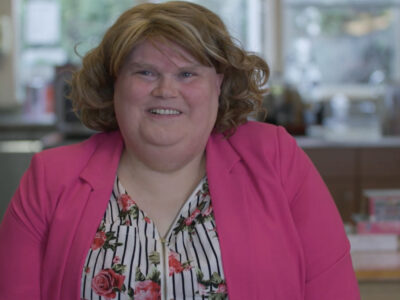 Leah-Nora smiling at the camera in a pink cardigan and a striped floral blouse
