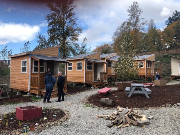 Image Description: Four people taking a tour outdoors during the fall season of an alternative village shelter site.