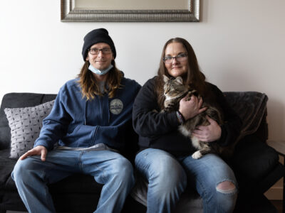 A man and a woman sit on a couch. The woman holds a cat.
