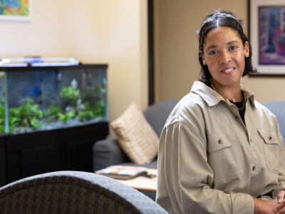 A woman sits in a waiting room in front of a fish tank and couches.