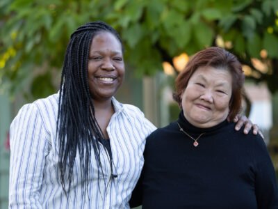 Two women stand next to each other outside.