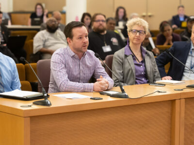 Four presenters from the Homeless Services Department sit at the dais in the boardroom.