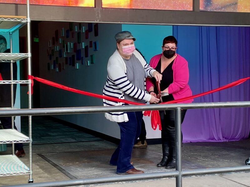 Two people cut a ribbon in front of a building